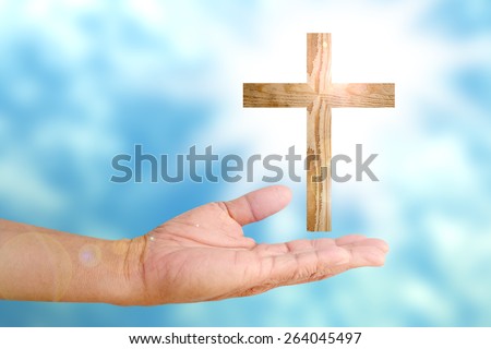 human hand presenting wood cross over bright light sun sky
