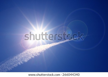 contrail cloud over blue sky and fairy sparkle sun with flare
