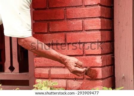 Brush in painter hand on brick pillar for color repair as shoot with slow speed to show movement