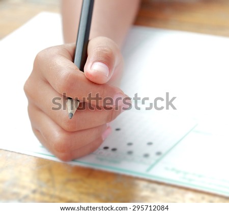 Little schoolgirl hand on examination answer sheet with black pencil in finger shot with wide aperture