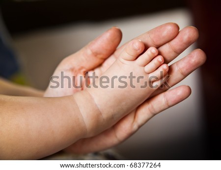 The 2 months female asian baby\'s right foot in her mom\'s left hand over blur background.
