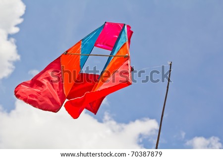 Light blue red and orange satin kite hanging over blue sky by bamboo stick and needle.