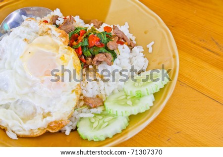 Glutinous rice in plate with fire egg cucumber and hot pork cooked on top place on natural yellow solid wood background.