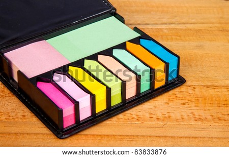 Multicolored post it note block in black leather case on wood table