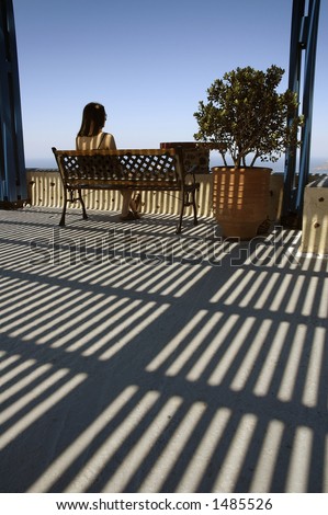 Young woman gazing out to see under a slatted shady veranda