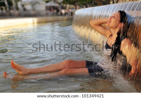 Woman enjoy the cold waters of  fountain during a heat wave. Concept photo of hot weather, heat wave, global warming, summer season, climate change,woman, enjoy life, free, freedom,happy, happiness.