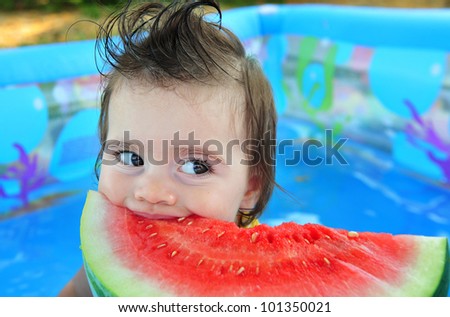 A baby girl eats a cold watermelon in a baby pool in a very hot day.Concept photo of hot weather, heat wave, global warming, summer season, climate change, child, enjoy life,happy, happiness, food.