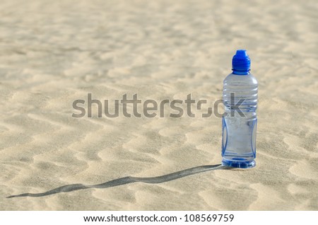 A cold bottle of water sitting in a sand dune in the desert.