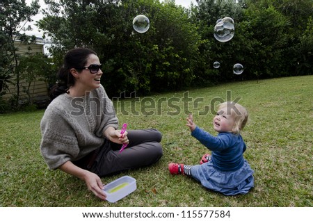 A mother and her little girl toddler play with bubble wand and mixture, in the garden outdoor. Concept photo mother and daughter relationship, love , care ,motherhood, parenting, relationship.
