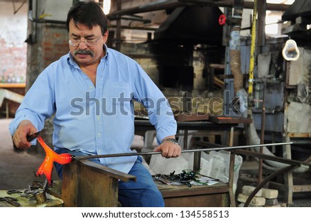 MURANO ISLAND - MAY 01 2011:Glassblowing artisan at work in a crystal glass workshop in Murano island Venice Italy.Murano glassmakers use the same tools as their ancestors have thousands of years ago
