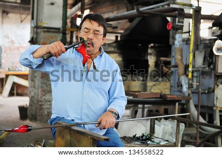MURANO ISLAND - MAY 01 2011:Glassblowing artisan at work in a crystal glass workshop in Murano island Venice Italy.Murano glassmakers use the same tools as their ancestors have thousands of years ago