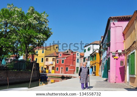 VENICE - MAY 01:Old woman outside here painted houses in Burano island on May 01 2011 Venice, Italy.Burano known for its painted houses and owners need special permit from the government to change it.