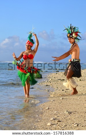 Portrait of attractive young Polynesian Pacific Island Tahitian male and female dancers in colorful costumes dancing on tropical beach during sunset.