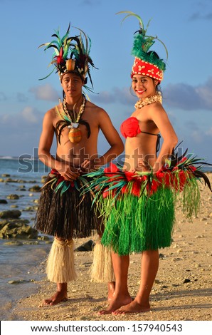 Portrait of attractive young Polynesian Pacific Island Tahitian male and female dancers in colorful costumes on tropical beach during sunset.