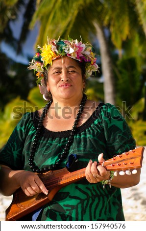 Portrait of mature Polynesian Pacific islanders woman sing and plays Tahitian Music with Ukulele guitar on tropical beach with palm trees in the background.