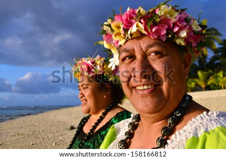 Portrait of two happy smily mature Polynesian Pacific islanders women on tropical beach with palm trees in the background.