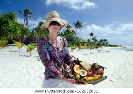 Young woman carry a tropical food of grilled fish, fruits and vegetables dish served on deserted tropical island in Aitutaki lagoon, Cook Islands.