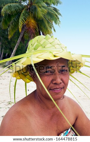 Portrait of Polynesian Pacific Island Tahitian mature female wearing here handcraft of a hat knees out of palm leaveson tropical beach in Aitutaki lagoon Cook Islands.