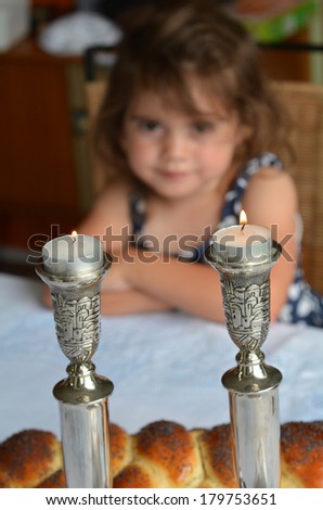 Jewish girl looks at lit sabbath candles before shabbat eve dinner.