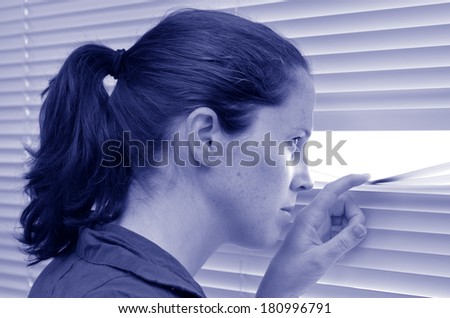 Young woman (age 25-30 ) looks out through Venetian blinds. Concept photo of curious, spy, nosy woman (BW).