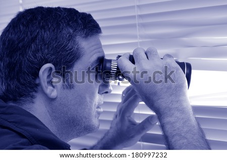 Man (age 35-40 ) looks and searches with binoculars and  looks out through Venetian blinds. Concept photo of curious, spy, nosy man (BW).
