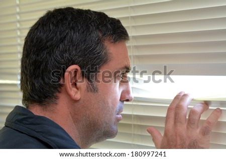 Man (age 35-40 ) looks out through Venetian blinds. Concept photo of curious, spy, nosy man.