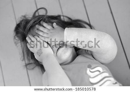 Abused little girl with a broken arm covering here face while crying. Concept photo of child abuse, violent in the family,domestic violent, social issues.