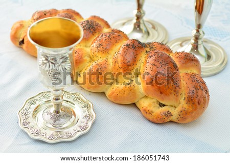 Shabbat eve table with uncovered challah bread, Sabbath candles and Kiddush wine cup.