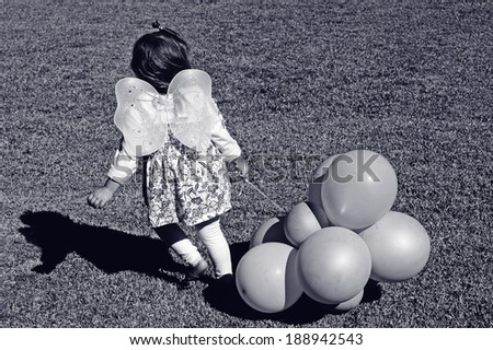 Little girl wearing angel fairy wings and hold ballon play pretend outdoor.