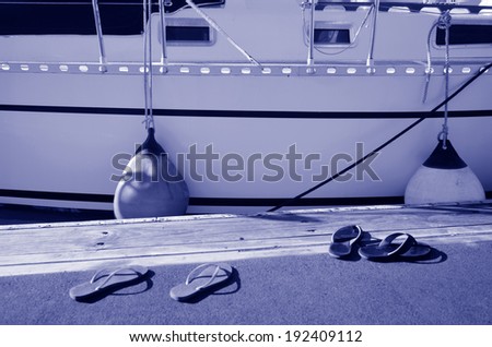 Flip flop shoes of a man and a woman beside a cruising yacht in the marina. Concept photo of Sailing, yachting and cruising lifestyle.