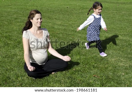 Pregnant woman meditate yoga exercise with her daughter during pregnancy outdoor at the park. Concept photo of women healthy life style and health care. copyspace