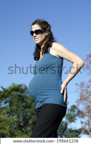 Pregnant woman suffers from back pains during pregnancy outdoor. Concept photo of women healthy life style and health care. copyspace