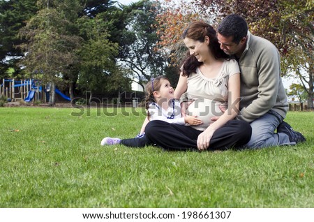 Pregnant woman been hug by her husband and daughter during pregnancy outdoor at the park. Concept photo of women healthy life style and health care. copyspace