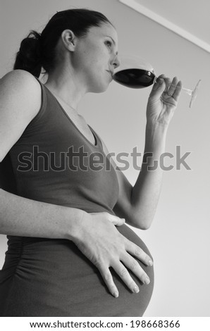 Pregnant woman drinks alcohol (red wine) during pregnancy .Concept photo of pregnancy, pregnant woman lifestyle and health care. copyspace (BW)