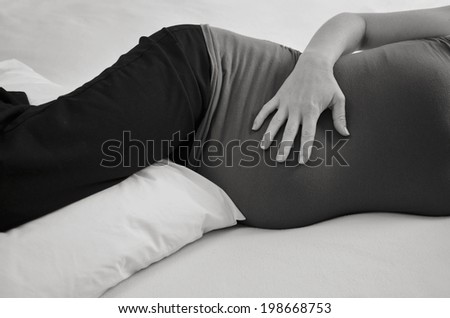 Pregnant woman lying with pillow on bed. Concept photo of pregnancy, pregnant woman lifestyle and health care.copyspace (BW)