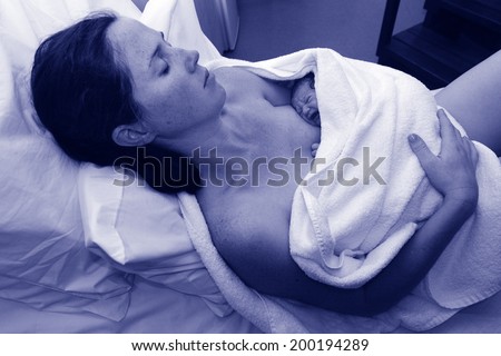 Mother rest with her newborn baby in bed immediately after a natural water birth labour. Concept photo of  pregnant woman, newborn, baby, pregnancy. (BW)