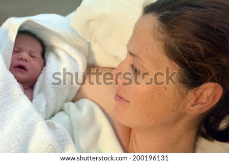 Mother looks at her newborn baby in bed immediately after a natural water birth labour. Concept photo of  pregnant woman, newborn, baby, pregnancy.