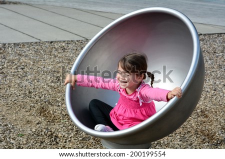 Little girl spinning on a  modern merry go round carousel at children toy playground in a park.