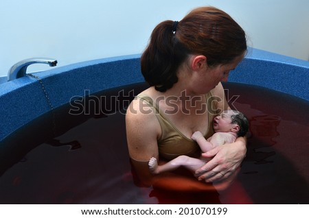 Young woman holds her baby in a pool after natural water birth.