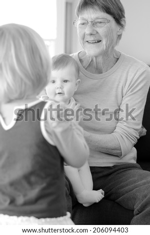 Happy grandmother play with her grandchildren at home. Concept photo of newborn, baby, grandmother, grand motherhood, senior,retirement, lifestyle (BW)