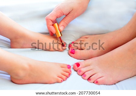 Young mother (30) and her girl child daughter (4 years old) paint their feet with nail polish together.