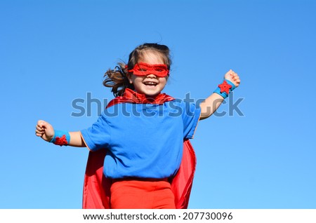 Happy Superhero child (girl) against dramatic blue sky background with copy space. concept photo of Super hero, girl power, play pretend, childhood, imagination.