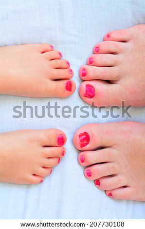 Young mother (30) and her girl child daughter (4 years old) compare the size of their painted nail polish feet.