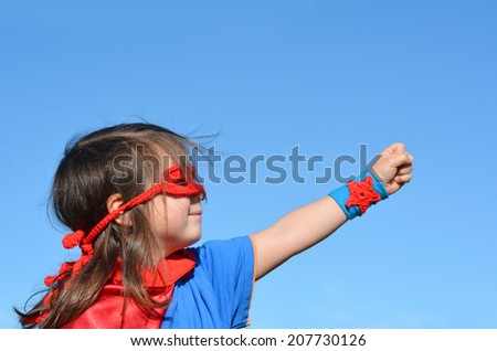 Superhero child (girl) against dramatic blue sky background with copy space. concept photo of Super hero, girl power, play pretend, childhood, imagination.