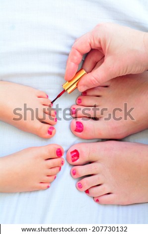 Young mother (30) and her girl child daughter (4 years old) paint their feet with nail polish together.