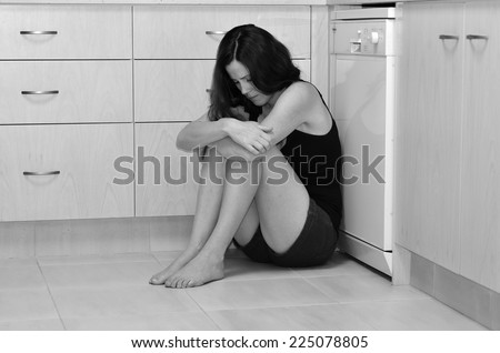 Sad woman sit in her kitchen and covering her face after domestic violence. (BW)