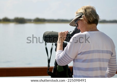 Mature woman birdwatching watching through binoculars in broadwater in Gold Coast Queensland, Australia.