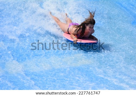 GOLD COAST OCT 29 2014: Young woman ride a surfing board on FlowRider. It is a water park attraction that simulate the riding of waves in the ocean