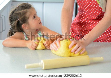 Mother show her child (girl age 05) how to knead dough in the kitchen.