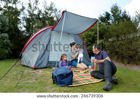 Young family, father and mother with two children camping in a tent outdoors.